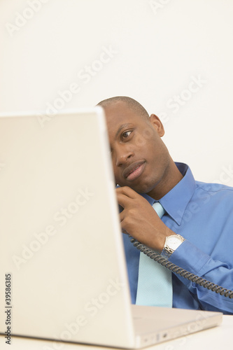 Photo: Businessman taking phone call and using laptop Businessman taking phone call and using laptop