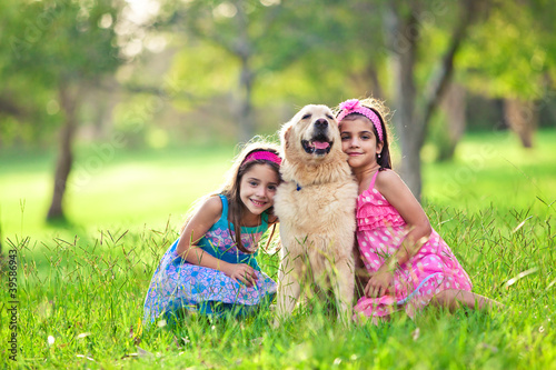 Photo: Two young girls hugging golden retriever in the park Two young girls hugging golden retriever in the park