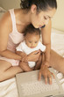 Mother holding baby and typing on laptop