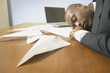 Businessman sleeping with paper airplanes on desk