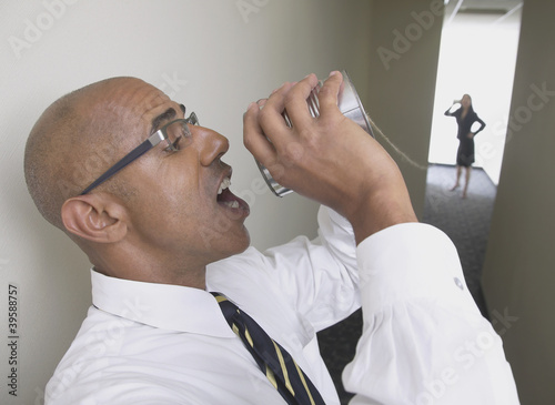 Photo: Profile of businessman talking through tin can to businesswoman Profile of businessman talking through tin can to businesswoman