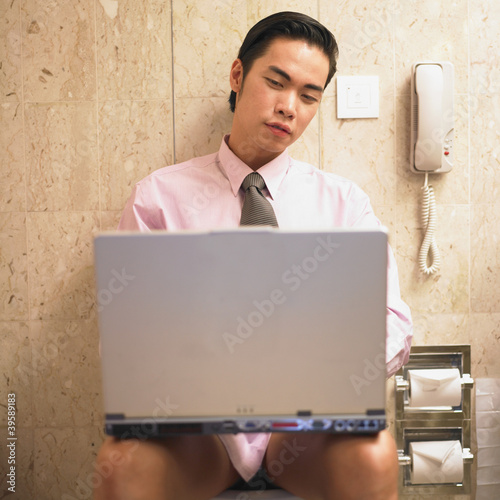 Photo: Businessman working on laptop while sitting on toilet Businessman working on laptop while sitting on toilet