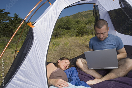 Photo: Woman sleeping in tent with man on laptop Woman sleeping in tent with man on laptop