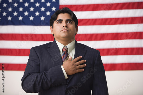 Photo: Businessman standing in front of an American flag with one hand across his heart Businessman standing in front of an American flag with one hand across his heart
