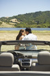 Couple kissing outdoors with convertible in foreground