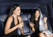 Two women drinking champagne in backseat of car