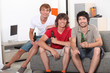 Three men sat on sofa holding bottles of beer Three men sat on sofa holding bottles of beer