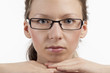 Auf Händen gestütztes Gesicht einer jungen Frau mit Brille
