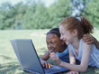 Two girls lying in park with laptop