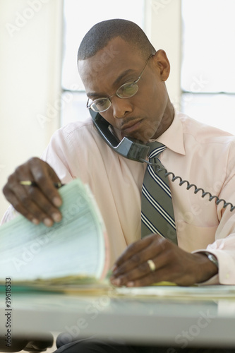 Photo: Businessman reading papers while talking on phone Businessman reading papers while talking on phone