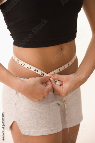 Photo: Mid section of girl measuring waist with measuring tape Mid section of girl measuring waist with measuring tape