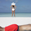 Young woman standing on the beach as boyfriend sunbathes