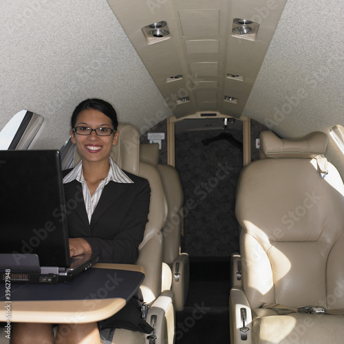 Photo: Businesswoman working on laptop inside airplane Businesswoman working on laptop inside airplane