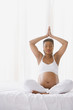 Pregnant African woman sitting on the bed doing yoga