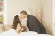 Hispanic man wearing a suit kissing Hispanic woman sitting in bed