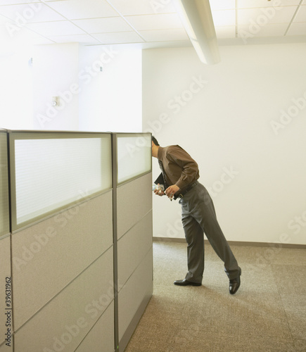 Photo: Businessman peeking around cubicle wall Businessman peeking around cubicle wall