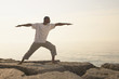 African man doing yoga on rocks at beach