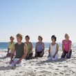 Group of women practicing yoga with instructor on beach