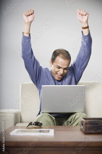 Photo: Indian man looking at laptop and cheering Indian man looking at laptop and cheering