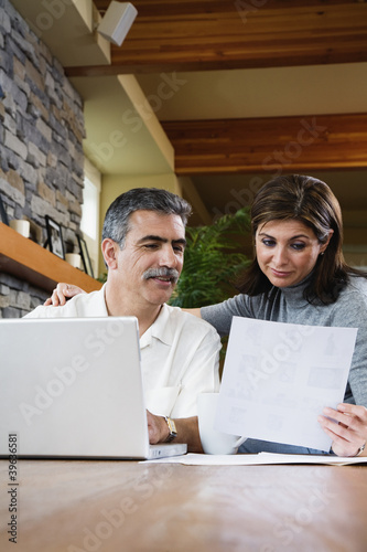 Photo: Middle-aged couple looking at paperwork and laptop Middle-aged couple looking at paperwork and laptop