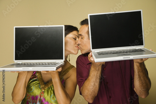 Photo: Hispanic couple kissing and holding laptops Hispanic couple kissing and holding laptops