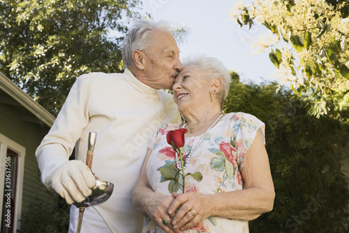 Photo: Senior man in fencing gear kissing wife Senior man in fencing gear kissing wife