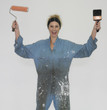 Woman wearing coveralls and holding paintbrushes