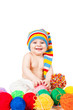 smiling baby in a hat plays with balls of yarn