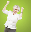 portrait of a cheerful senior woman gesturing victory over green
