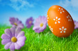 Orange easter egg in the grass against blue sky