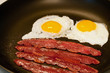 Eggs and bacon frying in a skillet