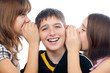 Two teenage girls sharing a secret with teenage boy