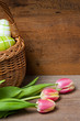 Osterkorb und Tulpen auf Holzbrett