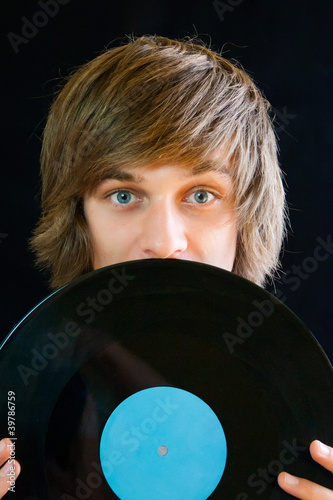 Photo: Portrait of a young man hiding behind a vinyl record Portrait of a young man hiding behind a vinyl record