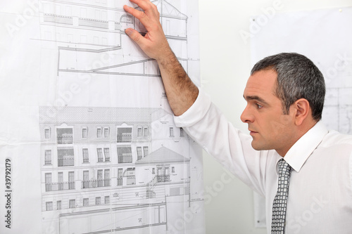 Photo: Architect looking at blueprints stuck to wall Architect looking at blueprints stuck to wall