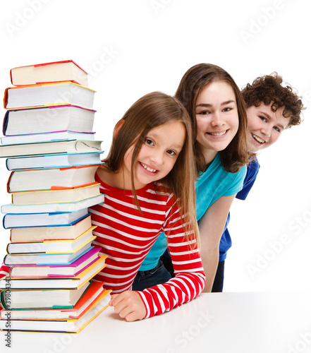 Photo: Students peeking behind pile of books on white Students peeking behind pile of books on white