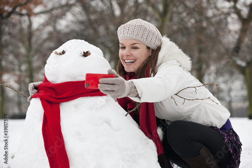 Photo: A young woman photographing a snowman A young woman photographing a snowman