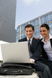 Business couple laughing in front of a laptop outdoors