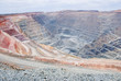 Big mine pit with little dump trucks and reddish soil