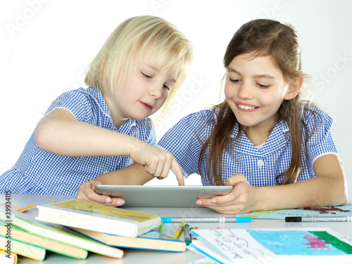 Photo: Two cute girlfriends learning with books and touchpad Two cute girlfriends learning with books and touchpad