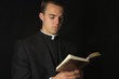 Young Priest in black reading prayer book