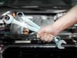 Close up of a hand with tools in front of an engine bay