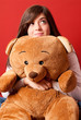 Young woman embracing teddy bear looking up sitting close-up
