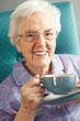 Senior Woman Relaxing In Chair With Hot Drink