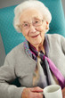 Senior Woman Relaxing In Chair With Hot Drink