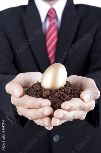 Foto: Businessman showing golden egg and soil Businessman showing golden egg and soil
