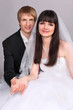 Happy groom and beautiful bride hold hands and look into camera