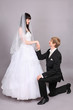 Happy groom kneels and holds beautiful bride hand in studio