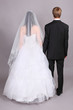 Groom and beautiful bride stand their backs to camera in studio