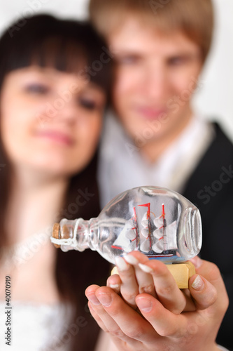 Foto: Happy beautiful bride and groom hold little vessel in bottle Happy beautiful bride and groom hold little vessel in bottle
